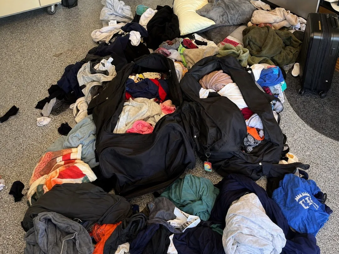 A sprawl of dirty camp laundry and open duffel bags across the floor