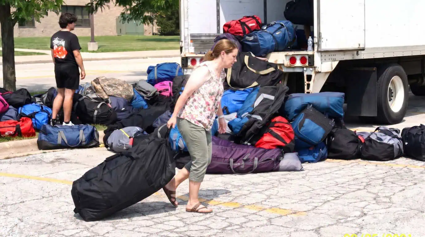 A parent dragging a heavy camp duffel bag across the driveway