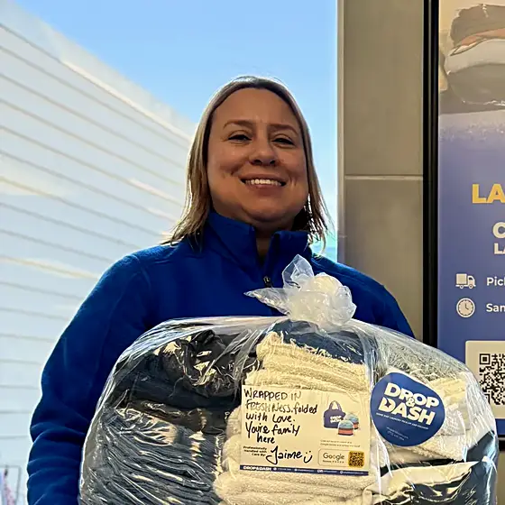 A smiling team member holding a finished order in front of a Drop & Dash poster