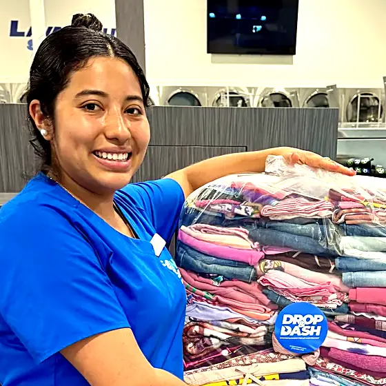 A smiling team member holding a wrapped stack of folded laundry
